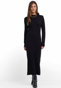 Czarna, dzianinowa sukienka z długim rękawem o dopasowanym kroju, z wysokim dekoltem i prostym dołem, w zestawieniu z czarnymi kozakami za kolano.