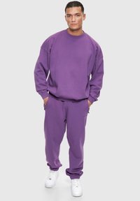 Lila Sweatshirt und passende Jogginghose aus weichem Material, mit lockerer Passform, gerippten Bündchen und Seitentaschen. Weiße Sneaker runden den Look ab.
