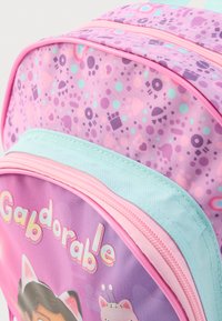 Roza in vijolična otroška nahrbtnik z grafičnim potiskom, več zadrgami in igrivimi vzorci, vključno s srcmi in oblikami. Mehka tekstura.