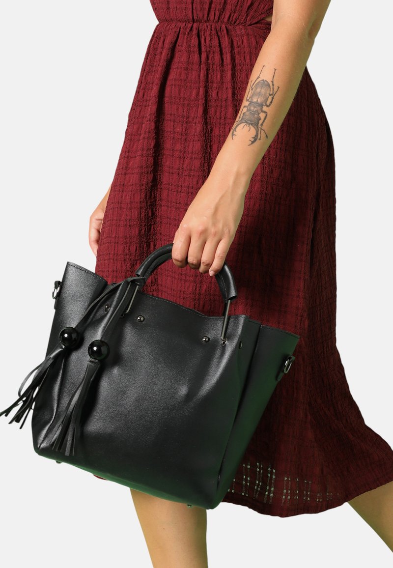 Svart läder tote-väska med en strukturerad form, som har två stora runda detaljer, fransar och silvriga metallaccenter.