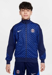 Veste zippée bleu marine présentant un motif géométrique en bleu clair, avec un col montant et le logo Nike sur la poitrine droite.