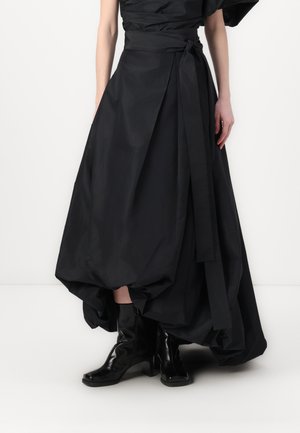 Falda negra y voluminosa con cintura atada, que presenta tejido en capas y drapeado. Combinada con botas negras hasta los tobillos con un tacón grueso.