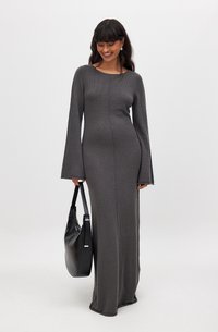 Robe longue ajustée en tissu gris foncé avec une finition texturée, dotée de manches évasées et d'une couture centrale. Le modèle porte un sac noir.