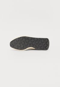 Black rubber shoe sole with a textured pattern, featuring a beige midsole. The design includes geometric shapes for traction.