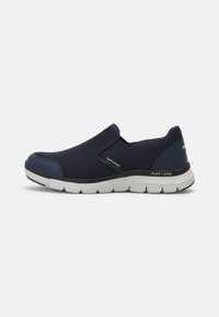 Tengerészeti kék slip-on cipők hálós felsőrésszel, kontrasztos sötét részletekkel és fehér párnázott talppal, amely rugalmas barázdákkal rendelkezik a kényelem érdekében.