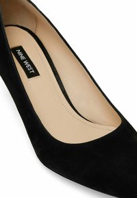 Scarpa nera in suede con tacco alto e punta arrotondata, con interno liscio. Presenta un taglio leggermente curvato lungo il bordo superiore e l'etichetta del marchio all'interno.