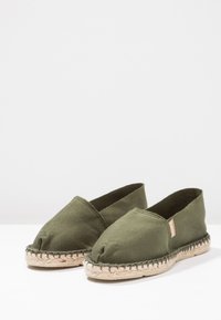 Green canvas espadrilles with a closed toe design, jute soles, and stitched detailing around the edges.