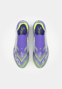 Purple soccer shoes with green accents, streamlined design, textured upper, and "F50" branding. Features a slip-on construction.