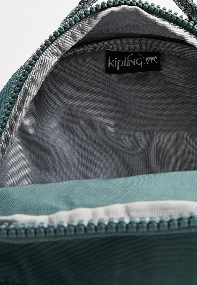 Bolsa de tela verde abierta que muestra un interior forrado en gris claro y una etiqueta negra de la marca "kipling" cerca de la abertura del zip.