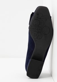 Chaussure en daim bleu marine avec une semelle en caoutchouc affichant des détails et motifs en relief. Présente un talon bas et un design de bout arrondi.