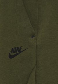 Mörkgrön kortärmad skjorta med ribbad textur och en tryckt svart Nike-logotyp. Har en liten accentdetalj nära logotypen.