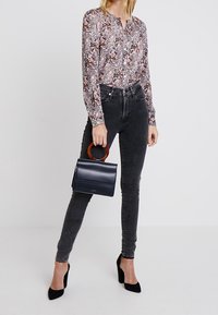 Blusa de manga larga con estampado floral en tonos de rosa y marrón, combinada con unos jeans ajustados gris oscuro y un bolso rectangular azul marino con asa de madera.