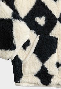 Pelsagt fleece-pullover med diamantmønster i sort og hvid, med et lille hjerte-motiv og hvide snorekanter。