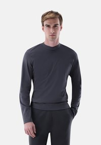 Dunkelgraues Langarmoberteil mit hohem Kragen, glatter Textur und tailliertem Schnitt, kombiniert mit passenden dunklen Hosen.