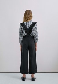 Pettorine nere con gambe ampie, caratterizzate da spalline arricciate. Abbinate a una camicetta a scacchi bianco e nero. Scarpe nere slip-on con borchie.