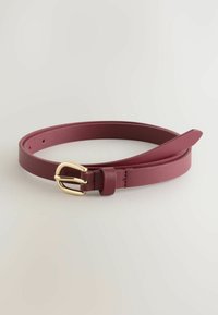 Cintura sottile in pelle bordeaux arrotolata con una piccola fibbia dorata e diversi fori di regolazione su uno sfondo neutro chiaro.