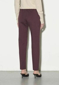 Pantaloni bordeaux con vestibilità slim e vita elastica. Tessuto liscio e orlo piegato, abbinati a sabot neri con tacco.