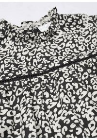 Halenka s leopardím vzorem v černobílé barvě, se nařaseným výstřihem, sklady a texturovaným povrchem.