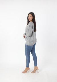 Maglione grigio oversize, jeans skinny blu e sandali con tacco trasparente. Tessuto morbido, vestibilità comoda, con dettagli a costine ai polsini e all'orlo.