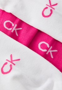 Calcetines de algodón blancos con una banda fucsia que presenta el logo "ck" en blanco. Textura suave, largo hasta la mitad de la pantorrilla y colores vibrantes en contraste.