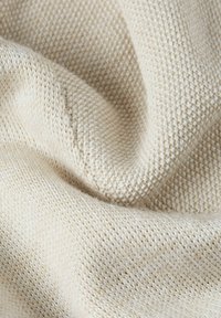 Helles beige Strickgewebe mit einer strukturierten Webart, das ein sanftes Erscheinungsbild und subtile Farb- sowie Faserabweichungen zeigt.