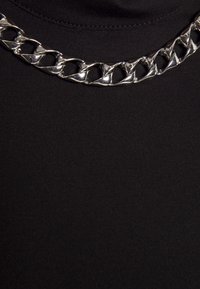 Collier chaîne épaisse en argent avec de gros maillons plats et entrelacés sur un fond en tissu noir.