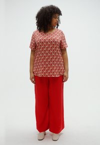 Κόκκινη μπλούζα με σχέδια και κοντά μανίκια, συνδυασμένη με κόκκινο παντελόνι φαρδιάς γραμμής. Το ύφασμα φαίνεται ελαφρύ με ομαλή υφή.