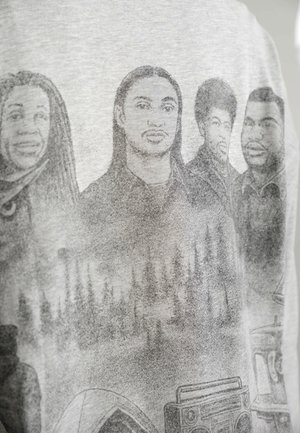 Graues T-Shirt mit einem monochromen grafischen Design von vier Figuren mit detaillierten Gesichtszügen und Accessoires, vor einem strukturierten Hintergrund.