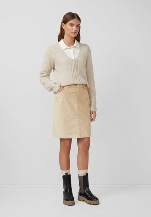 Beige gebreide trui met V-hals en ribbelstructuur, gecombineerd met een beige corduroy rok en zwarte enkellaarsjes met een dikke zool.