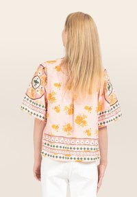 Blusa floreale rosa con maniche corte, caratterizzata da fiori gialli, dettagli verdi e rifiniture decorative. Tessuto leggero con una vestibilità comoda.