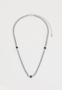 Collier en chaîne en métal argenté avec des maillons torsadés, présentant des accents noirs alternés et une chaîne ajustable pour varier la longueur.