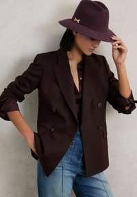 Dvořené vínové blejzr s saténovou černou košilí, spárovaný s světlomodrými džíny a tmavofialovým plstěným kloboukem se zlatým akcentem.