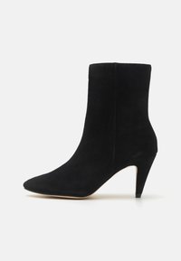 Bottine en daim noir avec un bout pointu et un talon aiguilles de 7,5 cm. Texture lisse et design minimaliste, avec des lignes épurées.