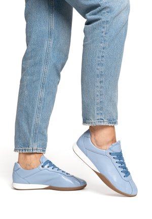 Hellblaue Ledersneaker mit abgerundeter Spitze, flacher weißer Sohle und kontrastierenden dunkelblauen Schnürsenkeln. Dazu hellblaue Jeans.