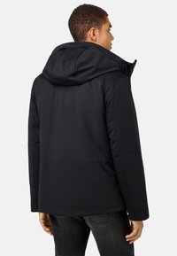 Melnā izolētā jaka ar kapuci, ar gludu tekstūru, strukturētu dizainu un sānu kabatām. Aizmugure ir bez apdares un gluda.