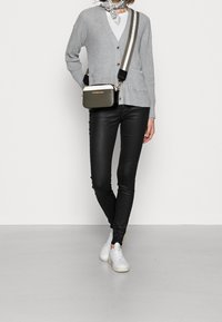 Grå ribbad cardigan över en vit topp, parat med svarta skinnybyxor och vita sneakers. Inkluderar en liten crossbody-väska med en kontrasterande design.