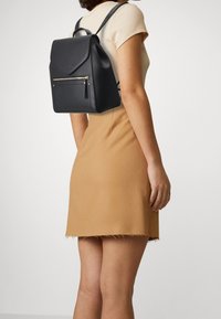 Black leather backpack with a flap design and a front zip pocket. Features adjustable shoulder straps and a top handle for carrying.