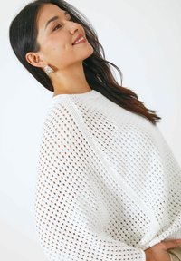 Pull en maille blanche, avec un tissage lâche et un grand motif en mailles ; il présente un col rond et des manches allongées.