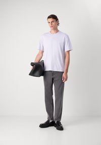 T-shirt violet clair à manches courtes, jeans gris à coupe droite et chaussures noires épaisses. Le mannequin tient un sac à main noir enroulé.