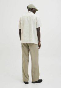 Chemise à rayures claires à manches courtes associée à un pantalon large beige et des chaussures noires ; modèle portant une casquette verte assortie.