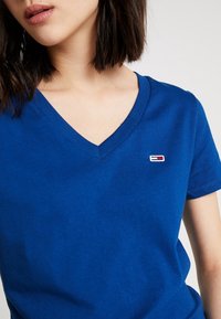 Blue cotton V-neck t-shirt featuring a small embroidered logo with red, white, and blue accents on the chest.
