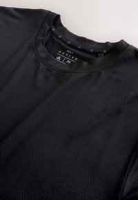 Black textured crew neck activewear shirt labeled "Next Active" in size medium, displayed flat on a light surface.