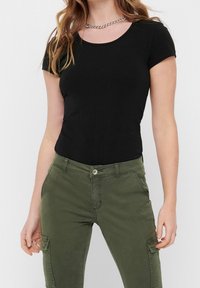 Svart kortärmad topp med rund halsringning, kombinerad med olivgröna cargobyxor med sidofickor och knäppning.