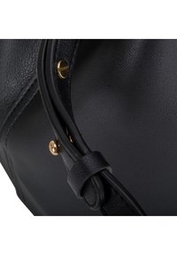 Gros plan sur un sac en cuir noir avec une bandoulière réglable et des détails de vis et rivets dorés.