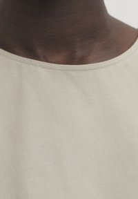 Gros plan sur le cou et le haut de la poitrine d'une personne portant un t-shirt uni beige clair à col rond.