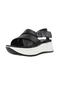 Sandali in pelle nera con cinturini incrociati e una fibbia circolare in argento, caratterizzati da una suola spessa bianca e nera per altezza e comfort.
