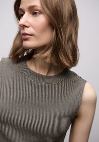 Bezrękawnik w prążki w stonowanych odcieniach zieleni i beżu. Posiada prążkowany dekolt oraz gładką strukturę. Subtelny detal na ramionach.