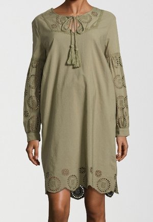 Robe olive longueur genoux avec manches longues en crochet, encolure ronde avec lien à pompons, et ourlet festonné avec motifs découpés circulaires.