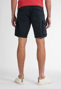 Mørkeblå cargo shorts med sidelommer, opbrudt kant og struktureret stof, parret med hvide sneakers med en tan hælaccent.