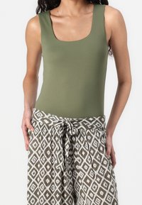 Olivgrön bodysuit med fyrkantig halsringning, kombinerad med mönstrade vida byxor som har en vit diamantdesign och en knut i midjan.